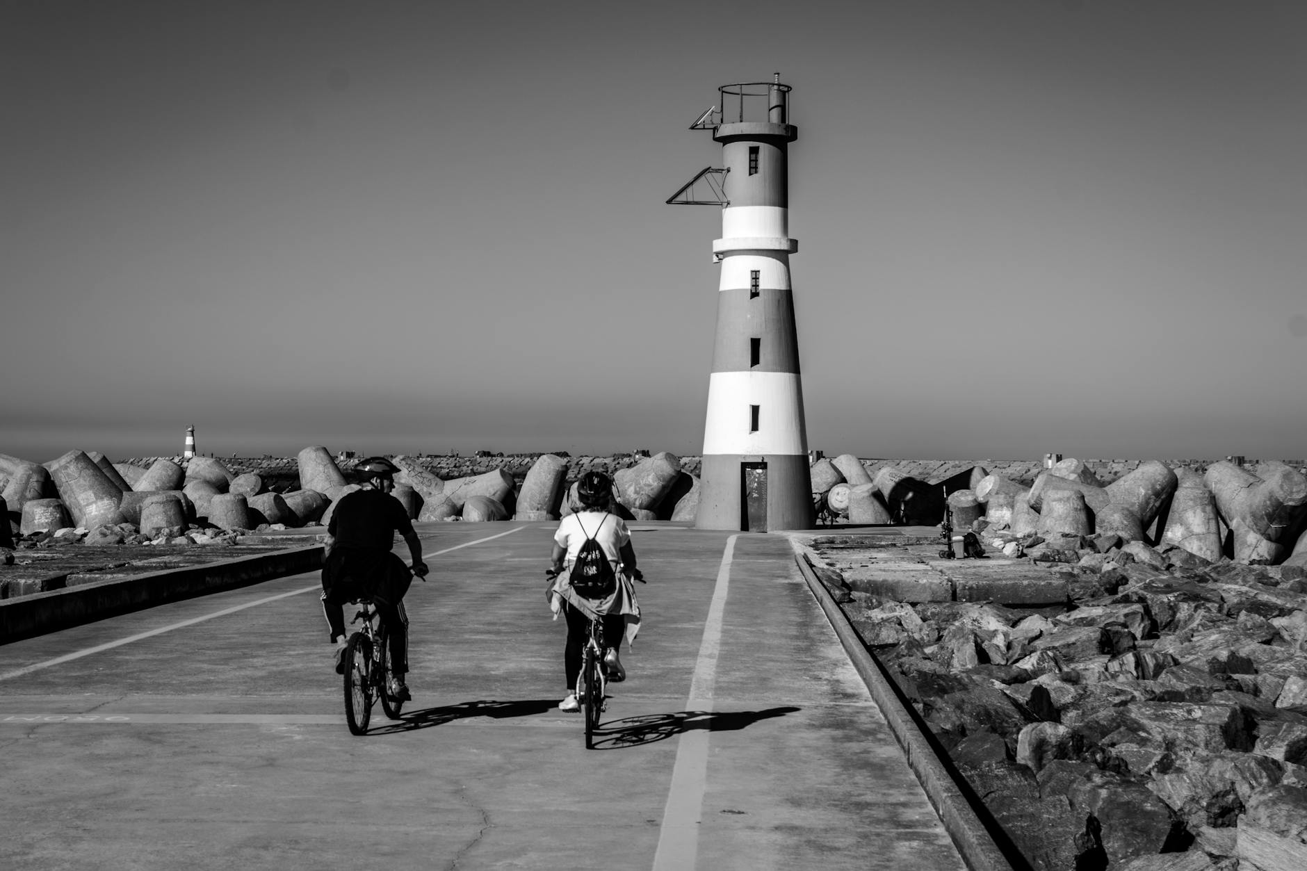Dwóch rowerzystów jedzie nadmorską ścieżką w stronę latarni morskiej