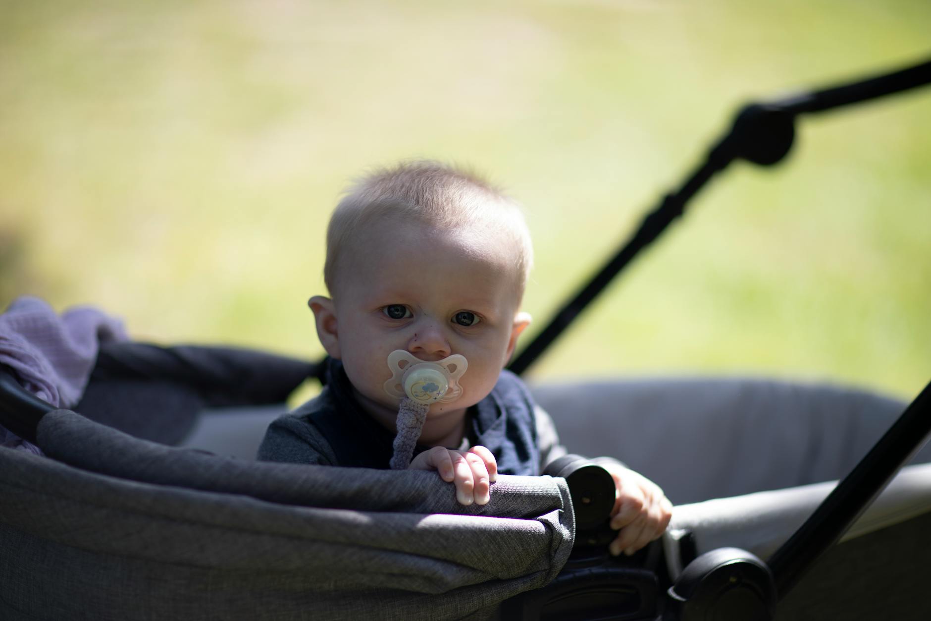 Niemowlę w wózku z smoczkiem na słonecznym spacerze w parku