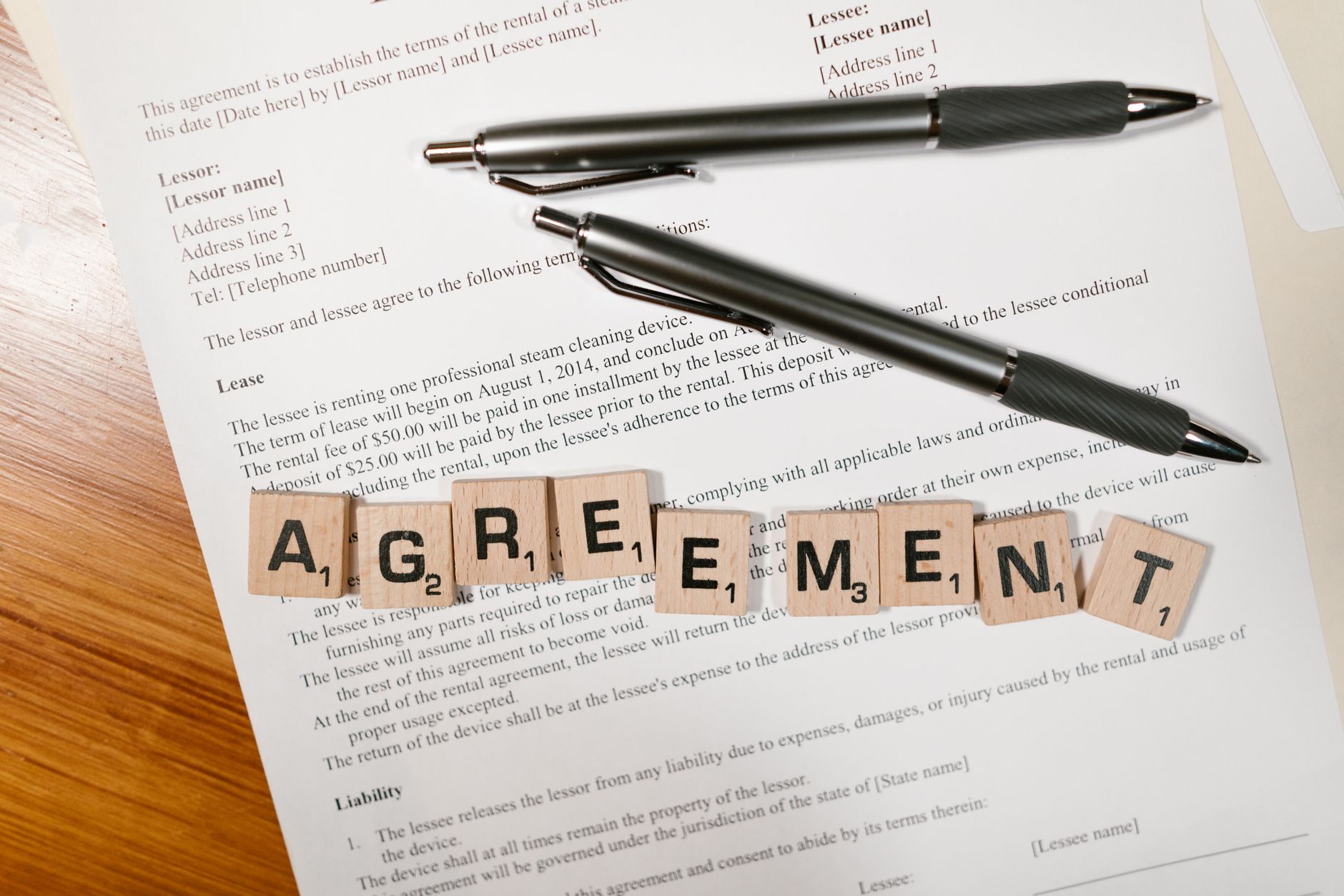 Dokument z napisem AGREEMENT ułożonym z literek Scrabble i dwoma długopisami