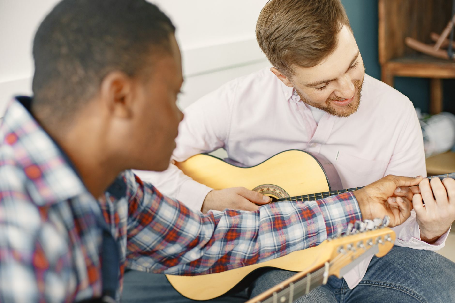 Nauczyciel pokazuje początkującemu mężczyźnie akordy na gitarze akustycznej