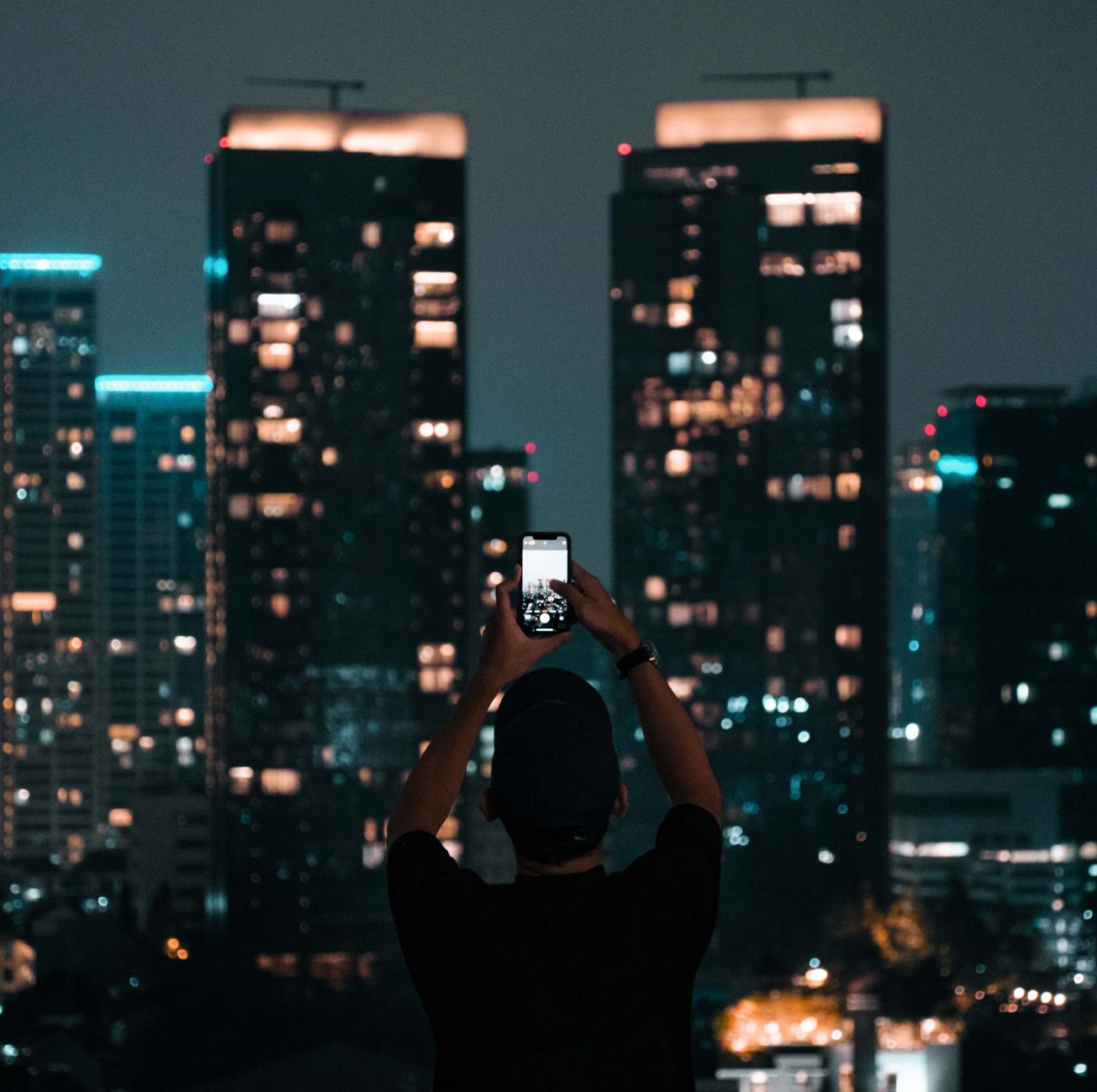 Osoba fotografuje nocną panoramę wieżowców w Dżakarcie