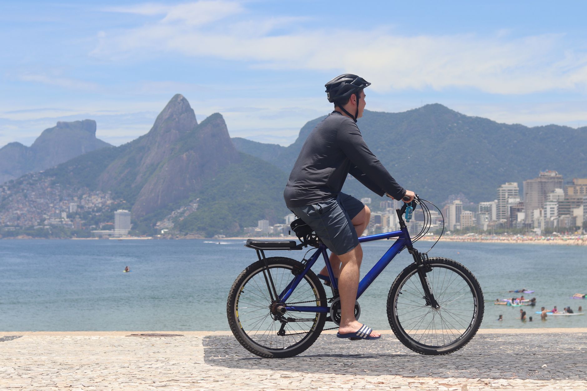 Brazylia dla aktywnych: trekkingi, surfing, nurkowanie i inne pomysły na urlop w ruchu Rowerzysta jedzie wzdłuż plaży Ipanema w Rio na tle gór latem